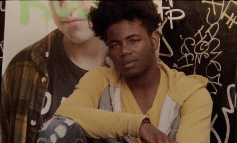 A black man sitting against a wall covered in graffiti