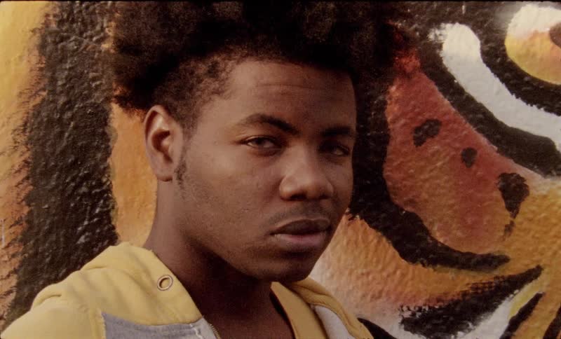 A young black man standing in front of a tiger mural staring intently ahead