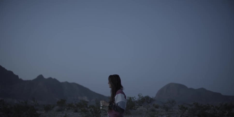A woman is standing in the desert drinking from a mug
