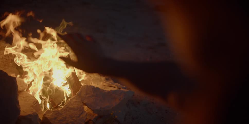 A person warms their hands by the fire at night