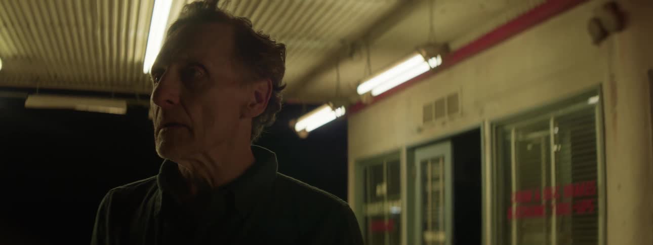 A man walking at night near a building and a red light shines on his face