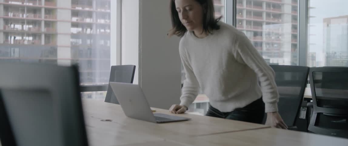 A woman finishes a phone call and sits at her desk to set to work on a laptop