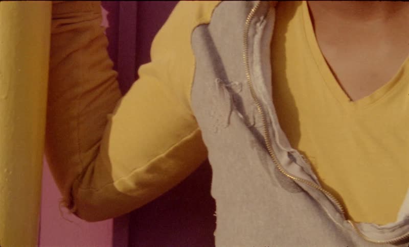 A black teenager stands outdoors with his hand resting on a yellow pole