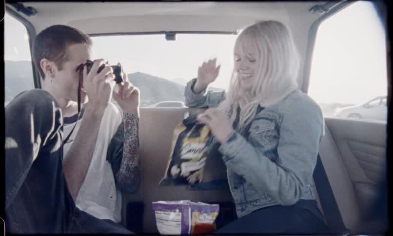 A guy takes a picture of a woman in the back of a car