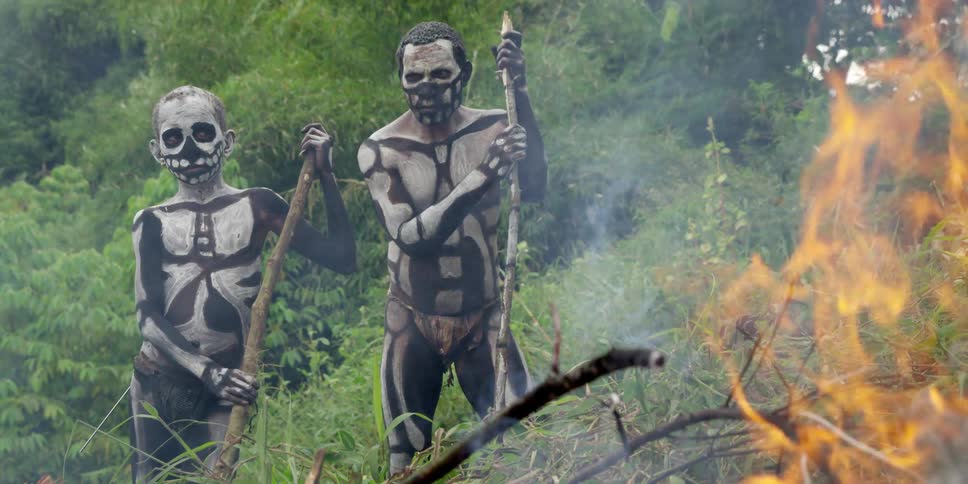 Native tribe members in full body paint standing next to a bonfire