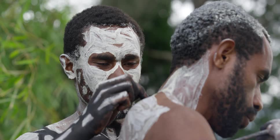 Indigenous man brushes paint onto another man