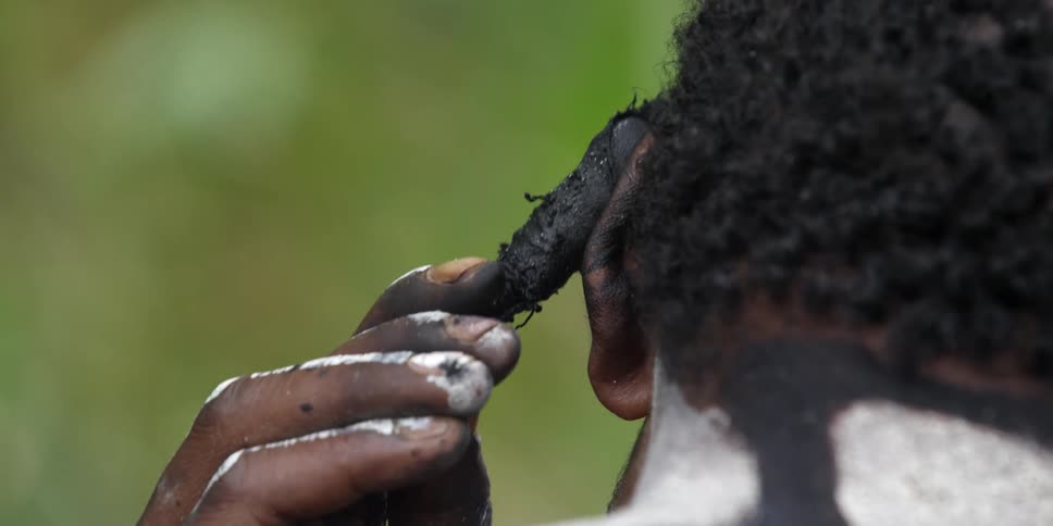 A man applying black paint to his ear