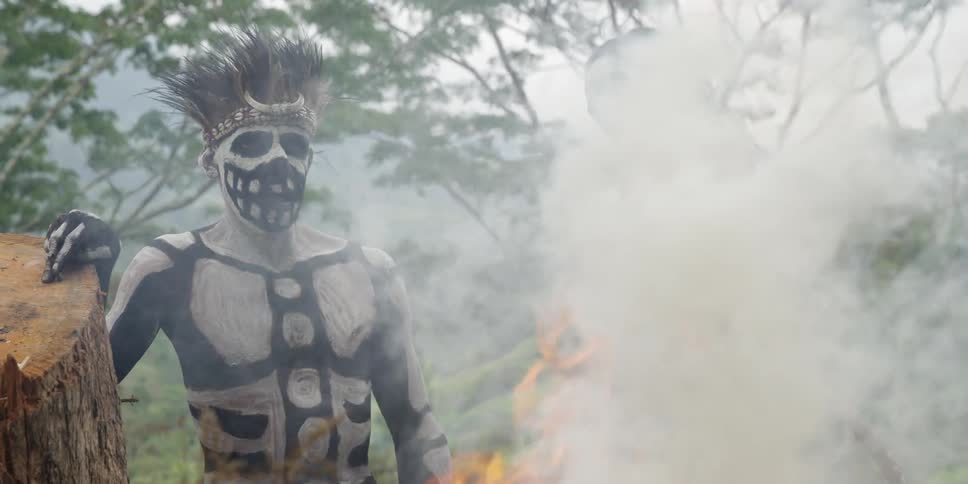 Painted tribal men standing before a fire