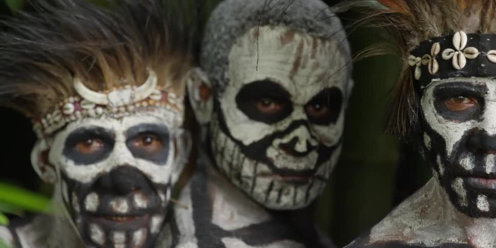 Native men in black and white paint costumes stand and stare