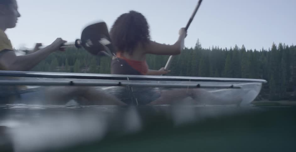 A man and a woman rowing in a paddle boat in calm waters surrounded by forest