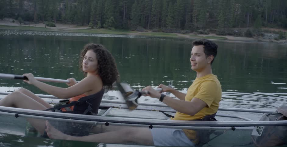 A couple riding a transparent kayak on a calm lake