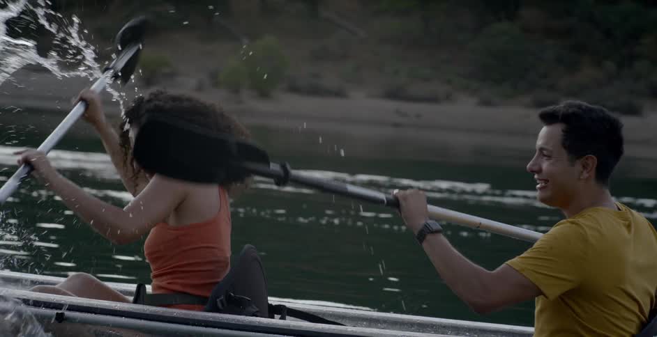 A man and a woman row a boat and splash each other with oars