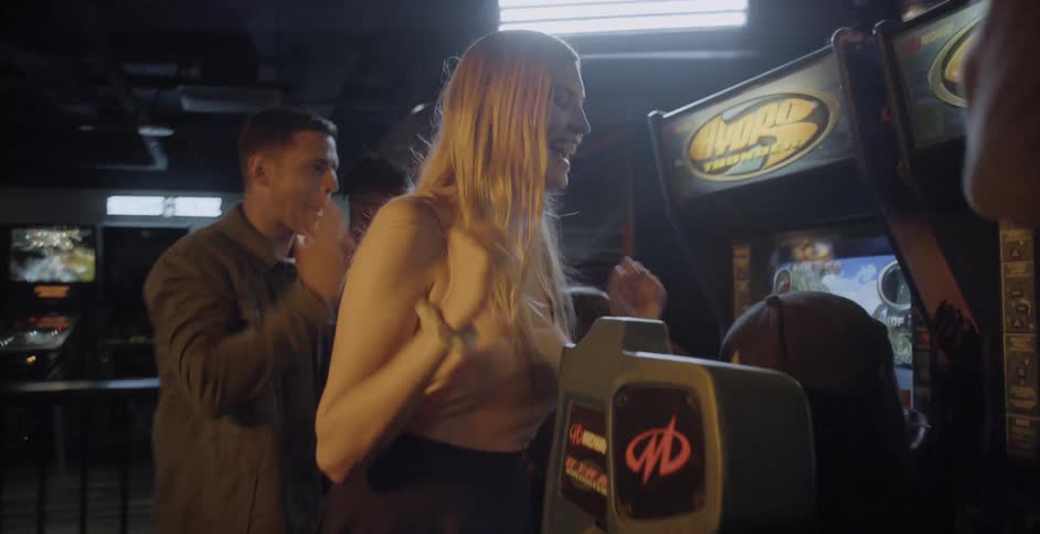 A group of young people cheering as someone plays a video game at an arcade