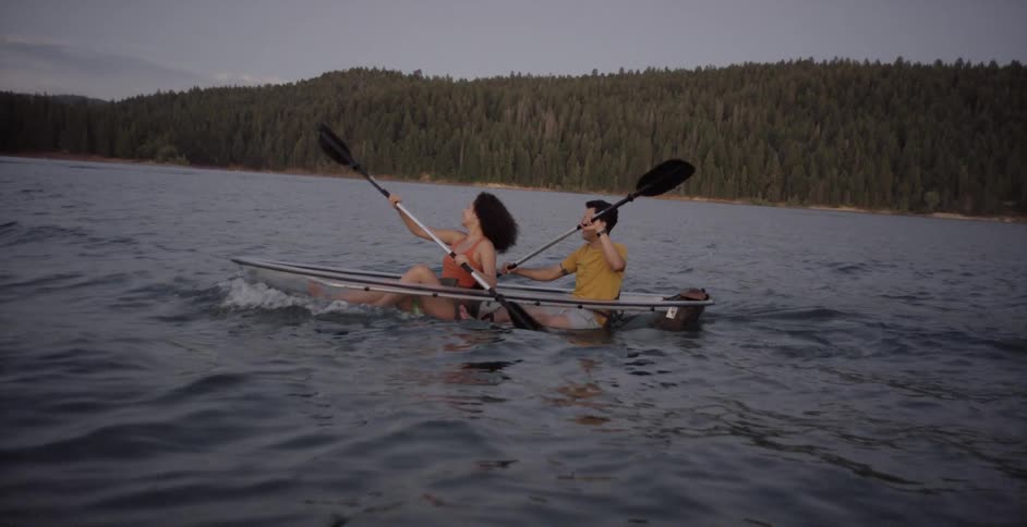 A young couple paddle a clear boat across a lake
