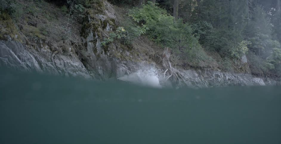 A caucasian male jumping off a steep hill into water