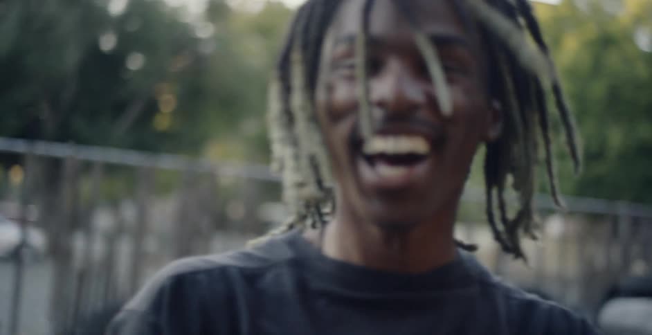 A young black man flips his hair around and laughs
