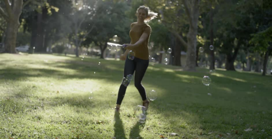 A young woman playing with a bubble wand in a park during the day