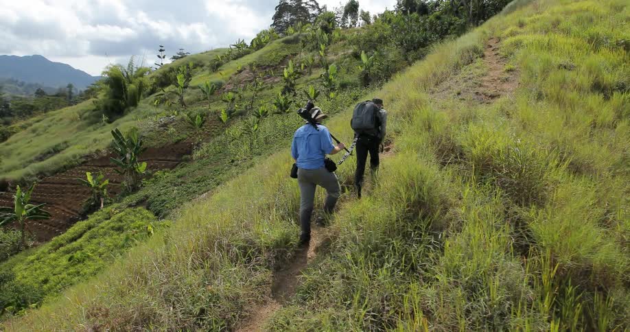 Two men hike up a hill on a narrow path