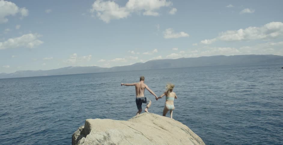 Couple jump off rock into ocean