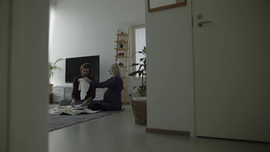 A man and pregnant woman look and baby clothes in the living room of a home