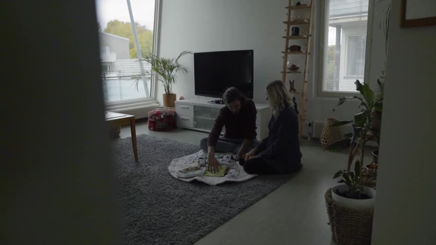 A young couple look at baby clothes while sitting on a rug in their living room