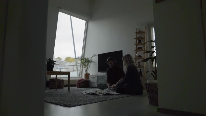 A female and male caucasian couple sitting on the living room floor folding baby clothes