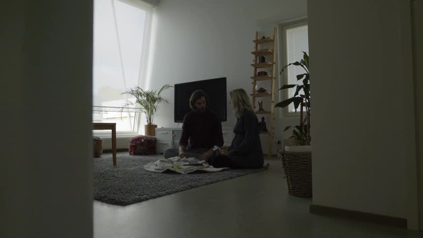 A man and a woman sitting on the floor looking at baby toys