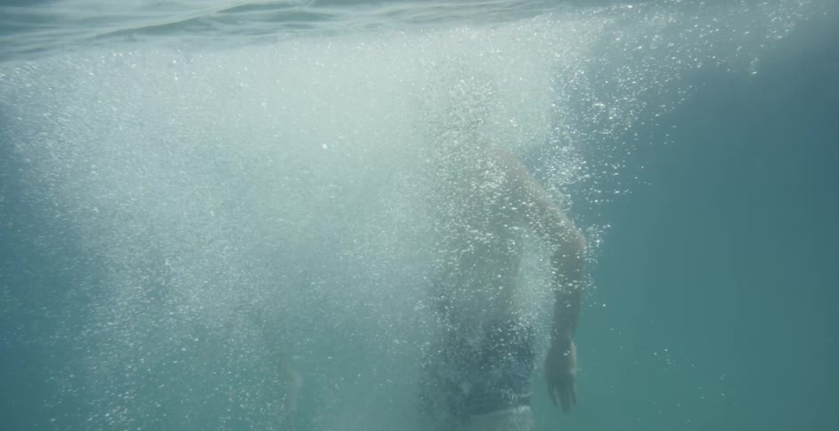 A caucasian male jumping into water and creating a lot of bubbles