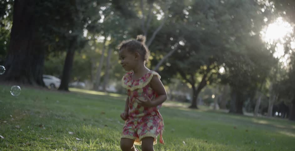 A young girl is running through the grass chasing bubbles