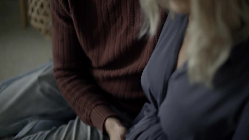 A man sitting next to and touching the stomach of a pregnant woman indoors