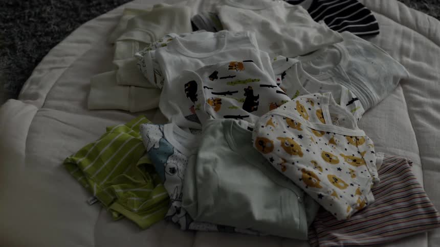 Someone looks at a pile of baby clothes