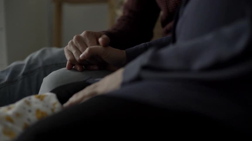 A man sitting indoors beside a pregnant woman