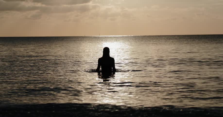 A woman dives up from under the water at sunset