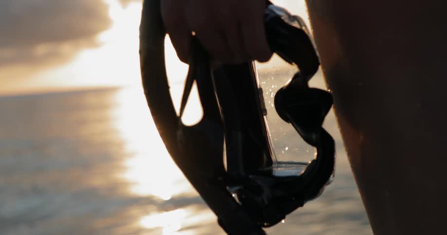 A swimmer holds snorkels filled with water having come out of the sea at sunset