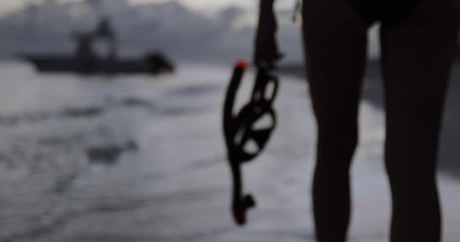 Awoman carries snorkeling gear towards the coastal waters