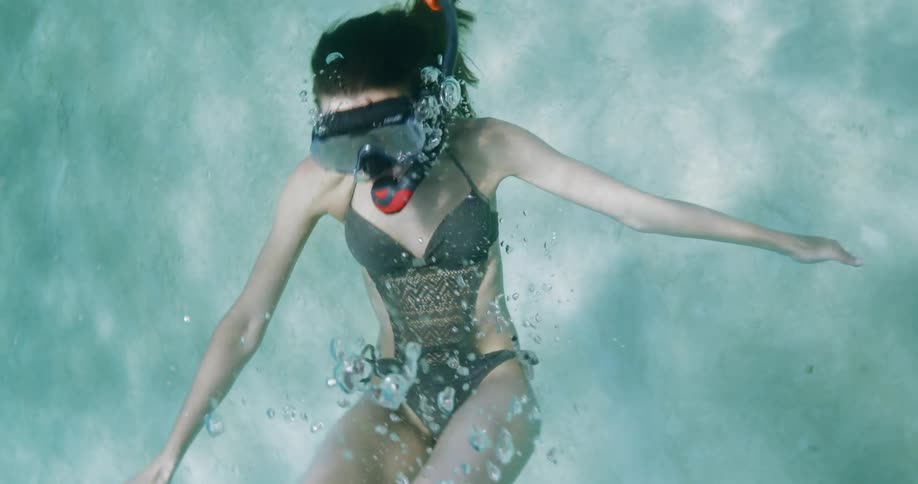 A female in a bikini in the water snorkeling and doing flips
