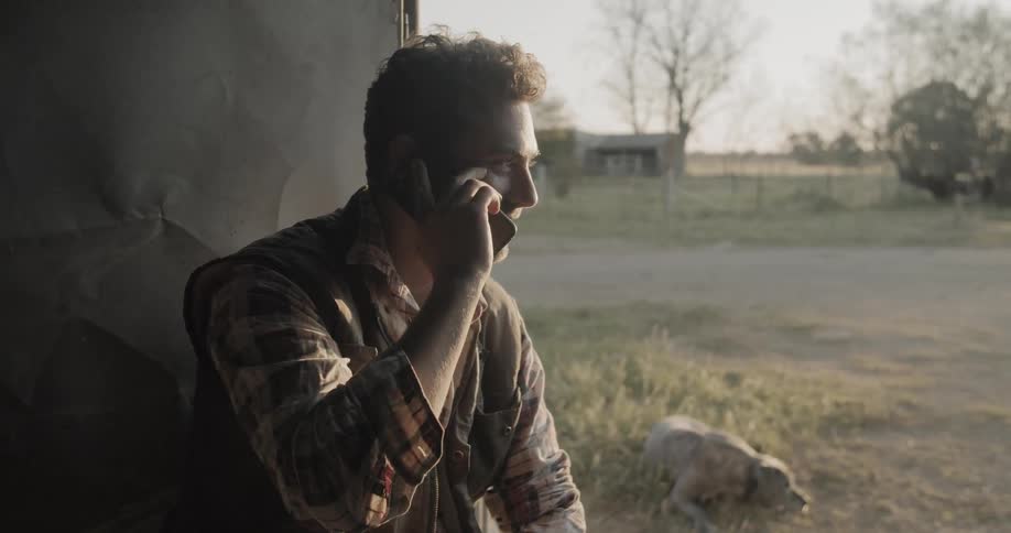 A white man sits outside and talks on a cell phone