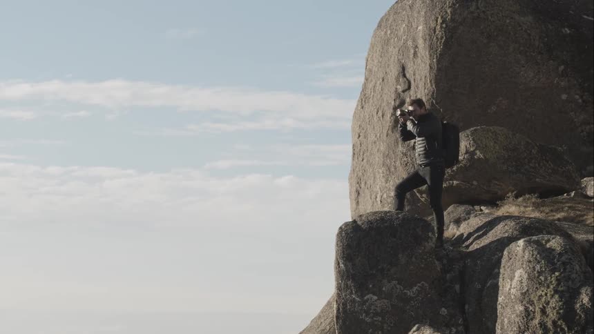 A man stands on a cliff and takes a picture with his camera