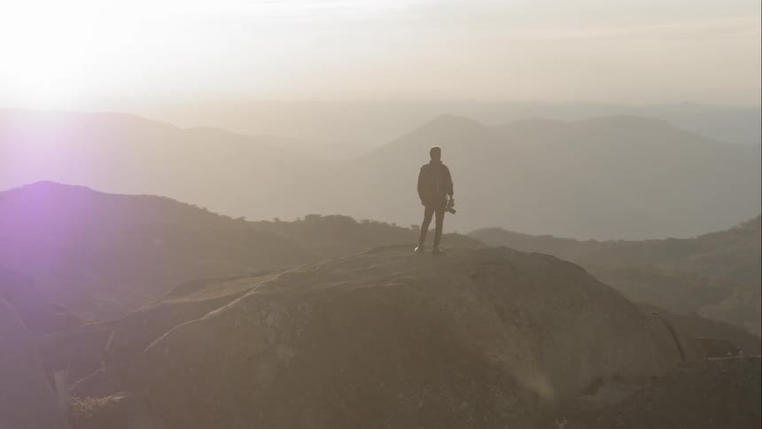 Aerial of a man standing on top of a mountain taking in the picturesque scenes