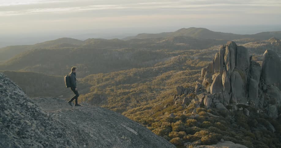 A hiker walking to the edge of a mountain and gazing at the valley below
