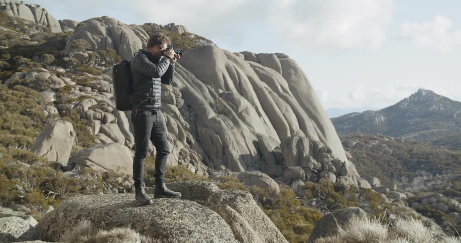 Man stands on rocky outcropping taking pictures of valley