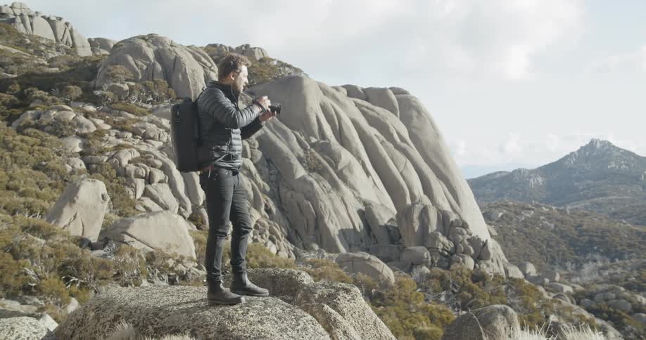 A man hikes through the mountains while taking pictures