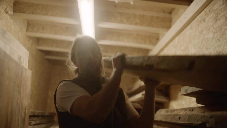 Blonde male picking out a slab of wood and carrying it out on his shoulders