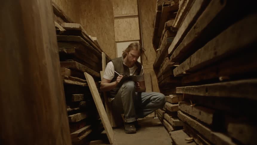 Man sits among wood supplies taking inventory