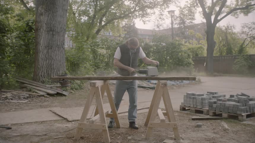 Contractor sanding a piece of lumbar outdoors near trees