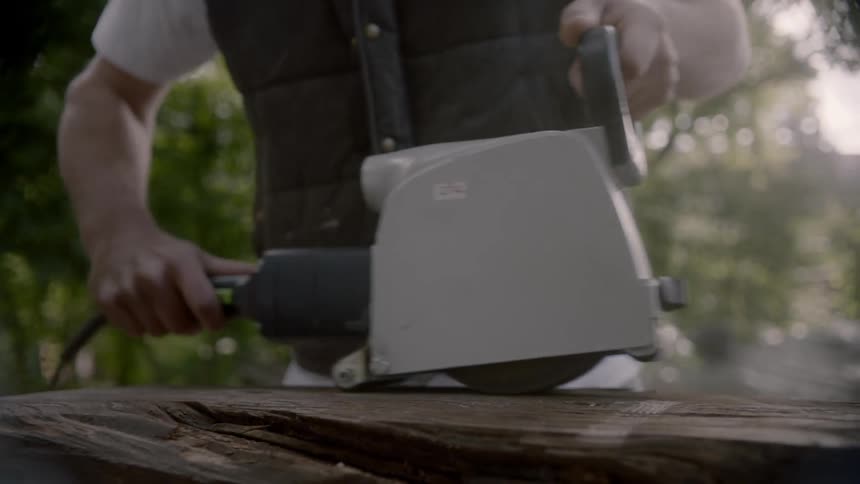 A man using an electric sander on a log outdoors during the day
