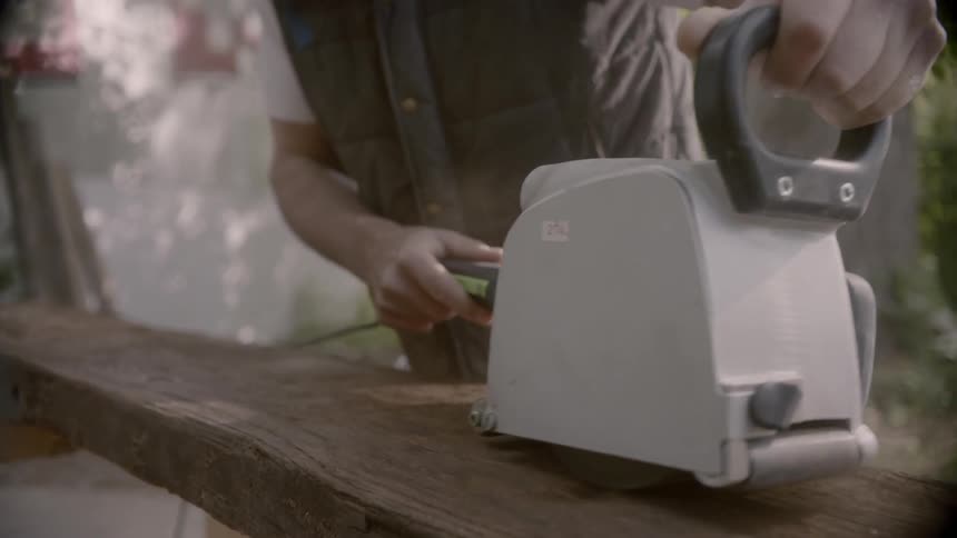 A man runs a power tool along a wood plank