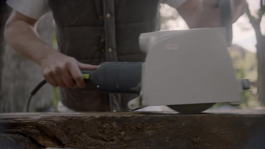 Man using a power tool to sand the surface of a rustic table