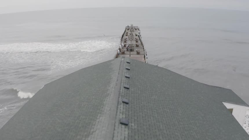 Flying over a pier that goes out into the ocean