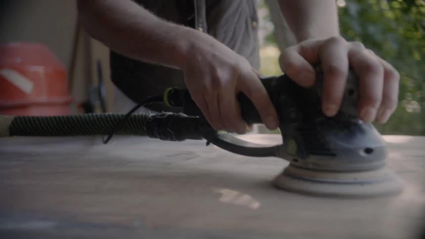 A man is using an electric sander on a piece of wood